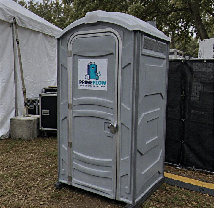 Grey portable restroom on asphalt beside event staging