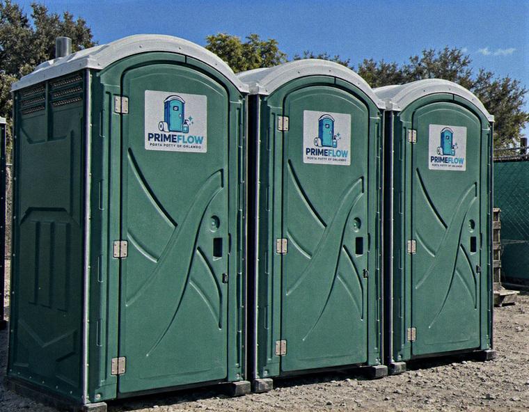 Three green portable restrooms lined up side by side at an outdoor event