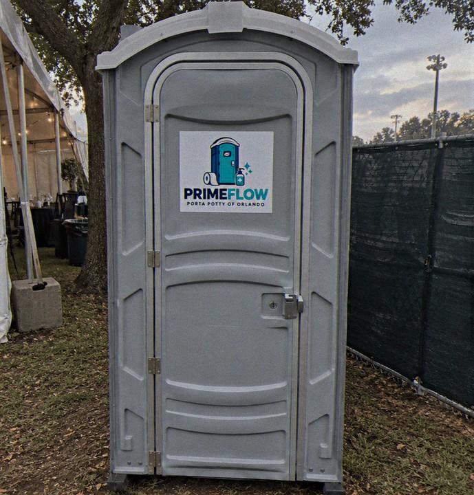 Standard grey portable restroom set up on grass beside an event tent
